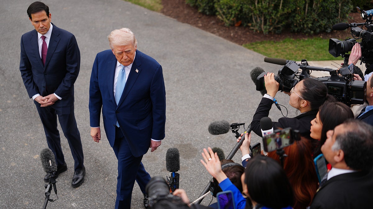 President Donald Trump speaking with reporters on the South Lawn as Secretary of State Marco Rubio listens.