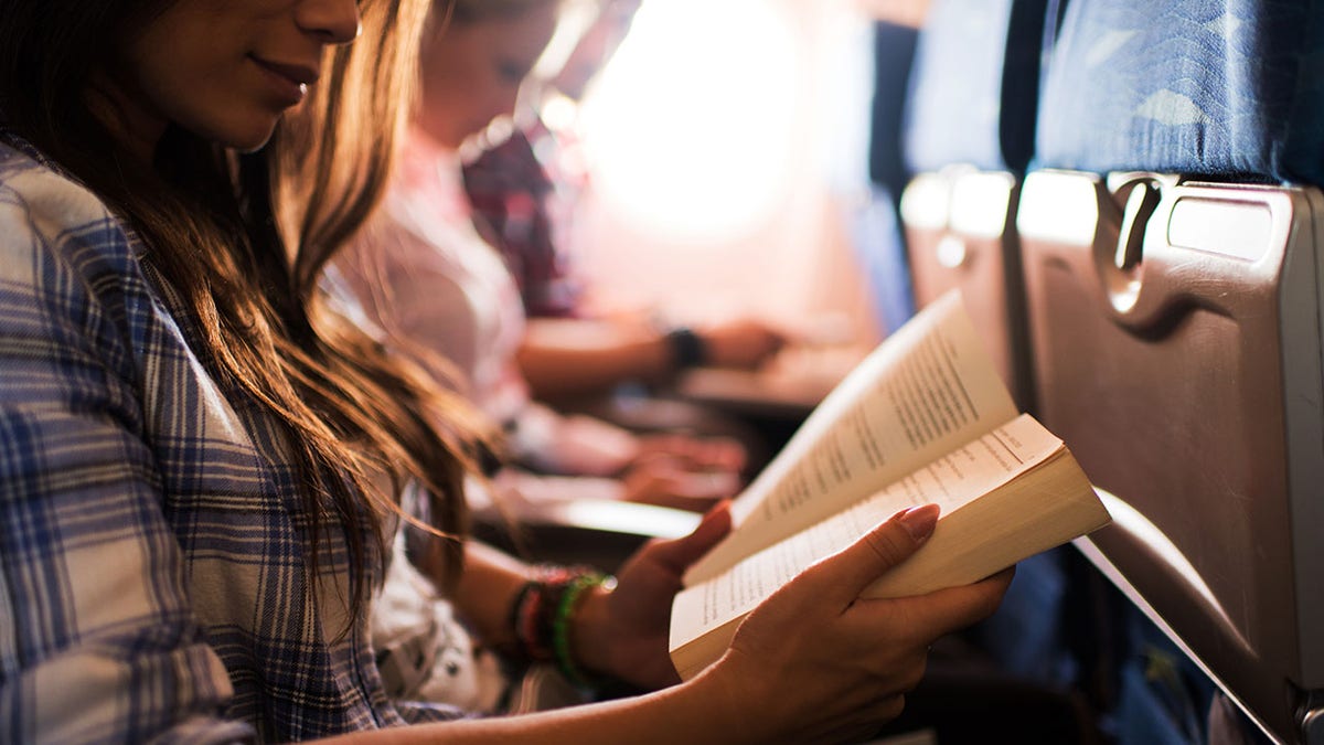 Unrecognizable woman smiling reading a book during her flight.