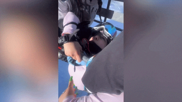 Skier dangling from chair lift while friends try and pull her up.