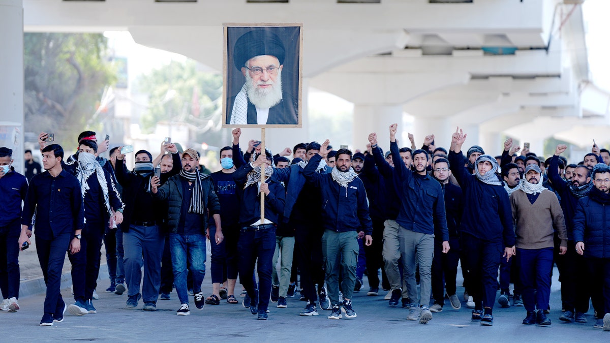 Protesters gathering in front of the Green Zone in Baghdad with posters and flags.