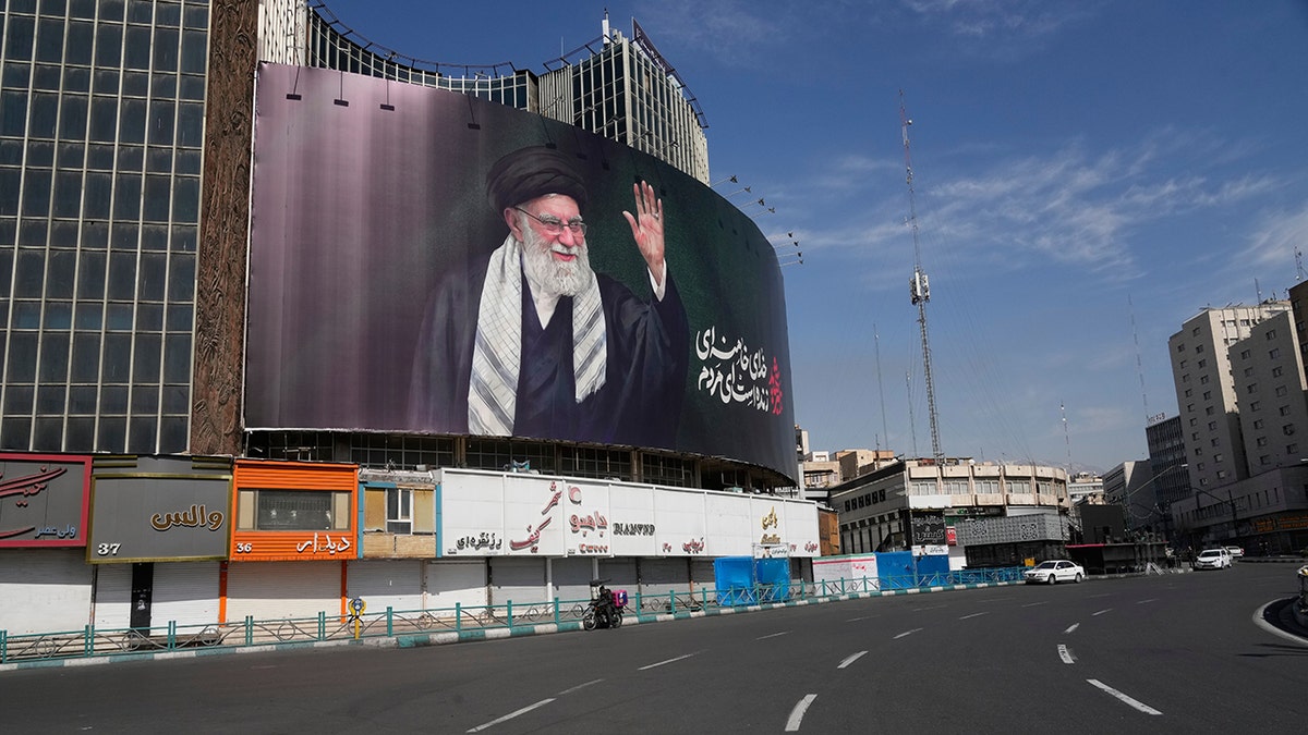 A billboard showing a portrait of the late Iranian Supreme Leader Ayatollah Ali Khamenei looming over an empty square.