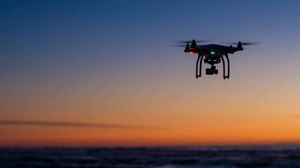 A stock image of a drone flying over the ocean at sunrise.