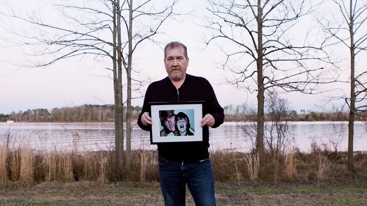 Timothy Jones Sr. standing in a field holding an old portrait of himself smiling with his young son Timothy Jones Jr.