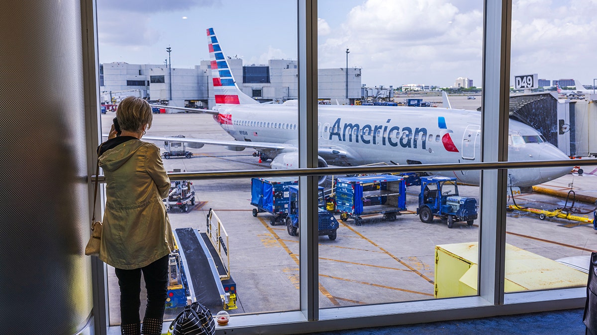 Woman talking on mobile phone at airport with American Airlines plane in background