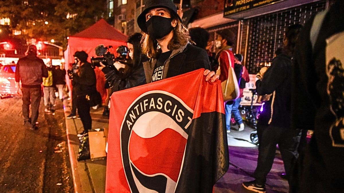 A masked demonstrator holding an anti-fascist banner at a protest in New York City