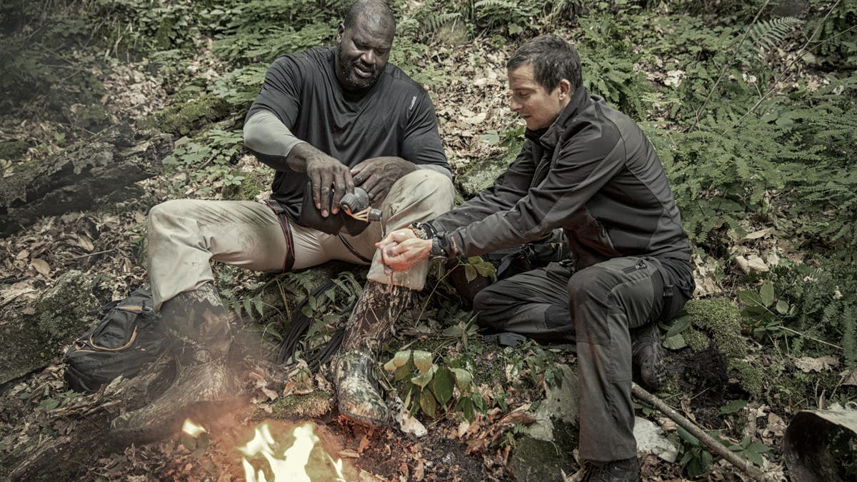 Bear Grylls and Shaquille O'Neal sitting at a bonfire during filming.