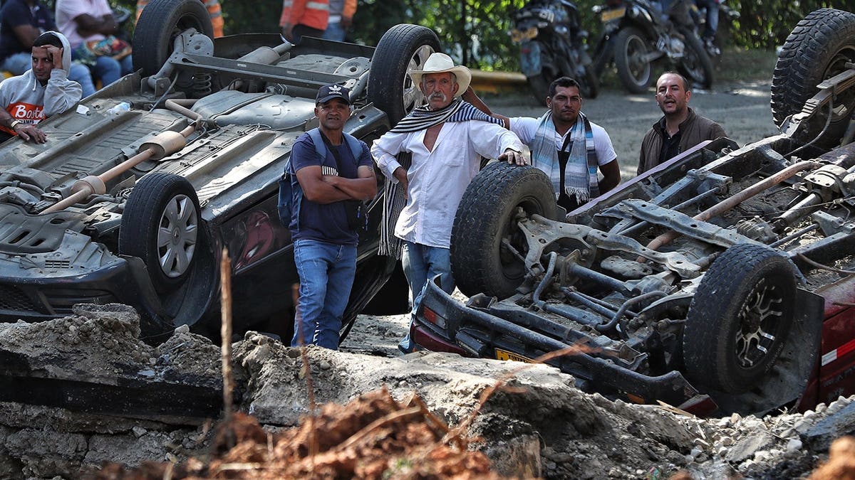 People look at vehicles damaged from an explosion.