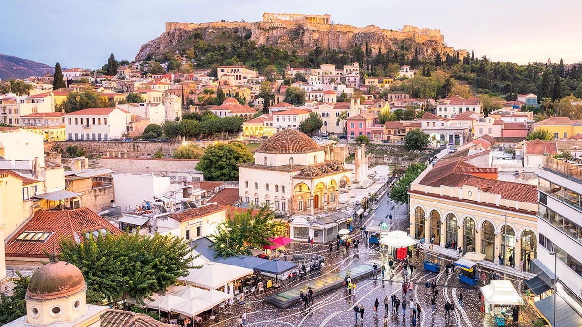 People walking in a square with the Ancient Greek Parthenon on the Acropolis in the background