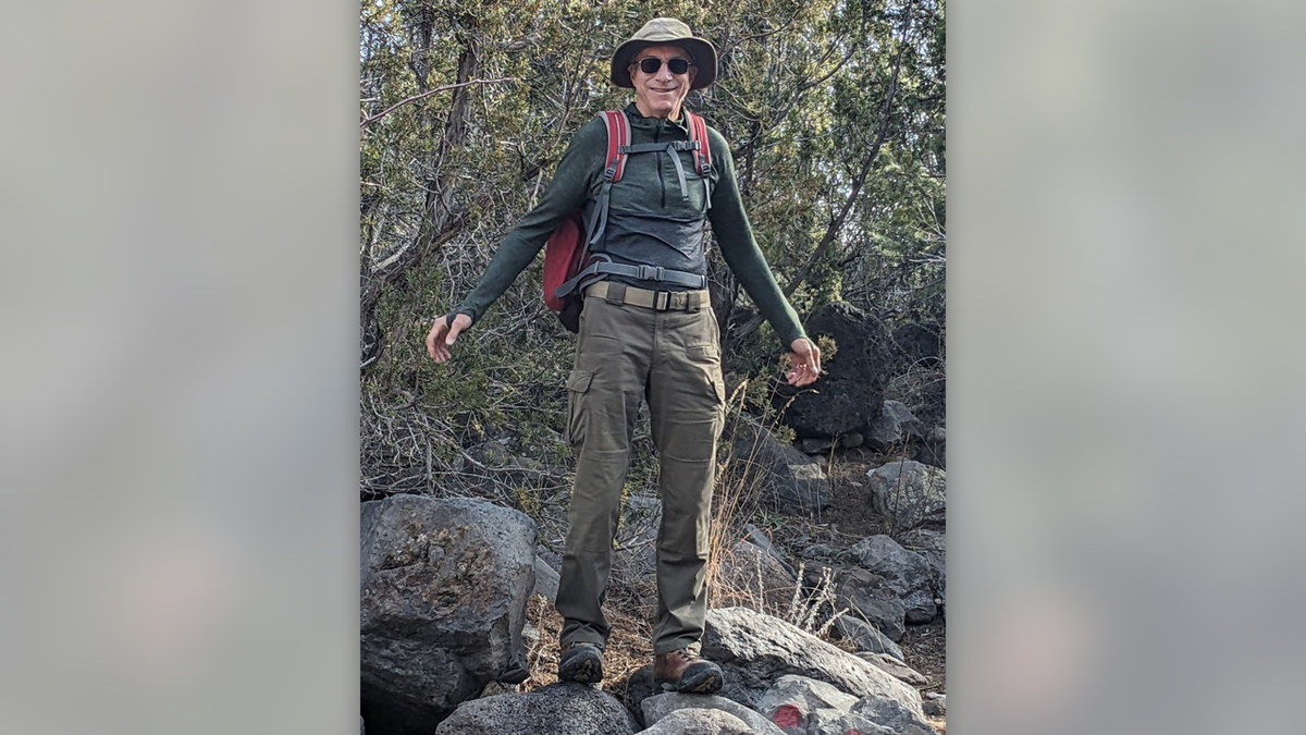 Retired Air Force Gen. William Neil McCasland in hiking gear atop boulders.