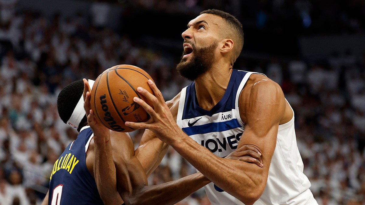 Rudy Gobert of the Minnesota Timberwolves is fouled by Justin Holiday of the Denver Nuggets during a basketball game.