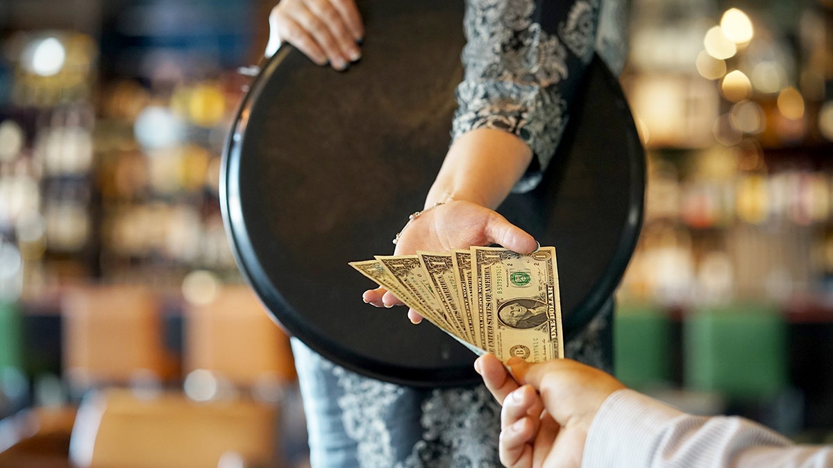 A waitress hand holding a serving tray receiving a five dollar cash tip from a customer