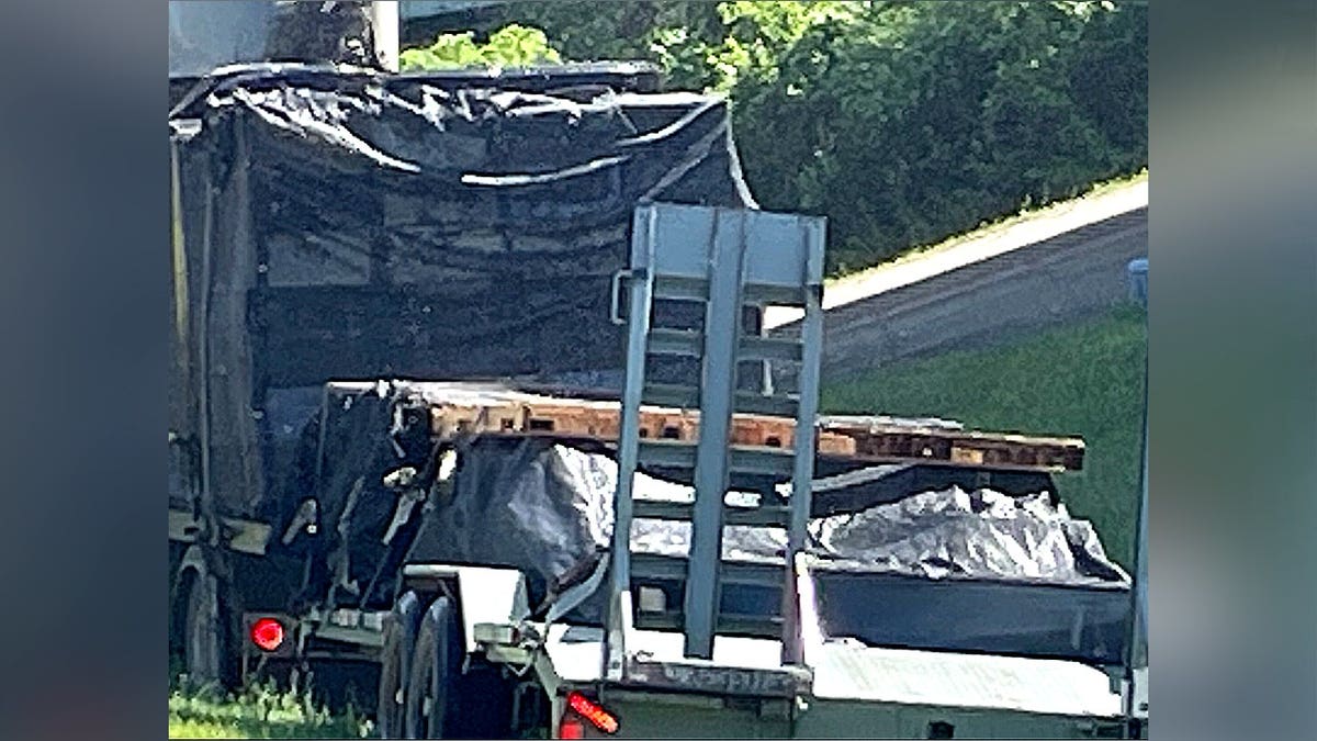 A close-up view of a damaged flatbed trailer with black mesh coverings and wooden pallets on the side of a road.