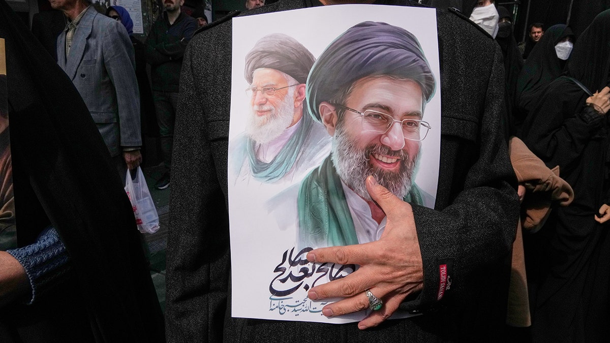 A mourner holding a poster depicting Ayatollah Mojtaba Khamenei and Ayatollah Ali Khamenei during a funeral procession in Tehran