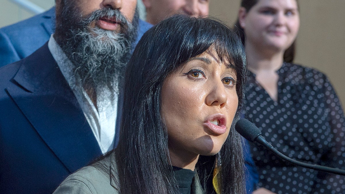 Leah Gazan speaking into a microphone while standing in front of several people.