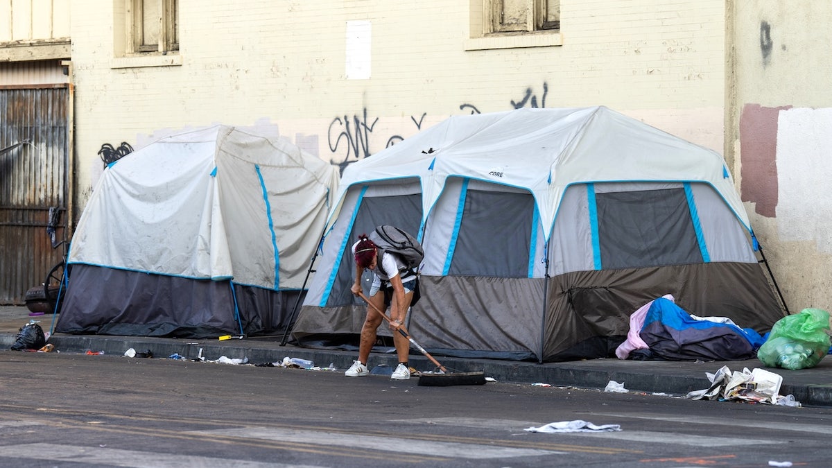 A homeless person clearing rubbish at a homeless camp on a sidewalk in Los Angeles