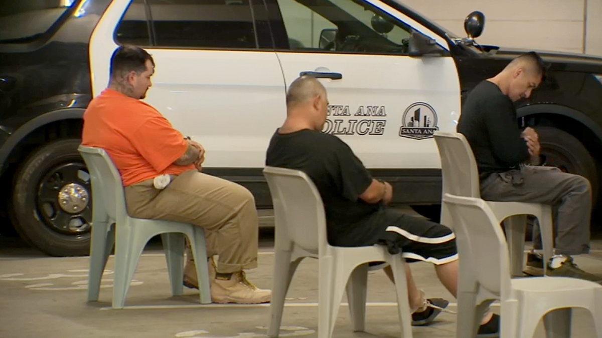 Mexican Mafia suspects sit detained in chairs near Santa Ana police vehicle during federal operation
