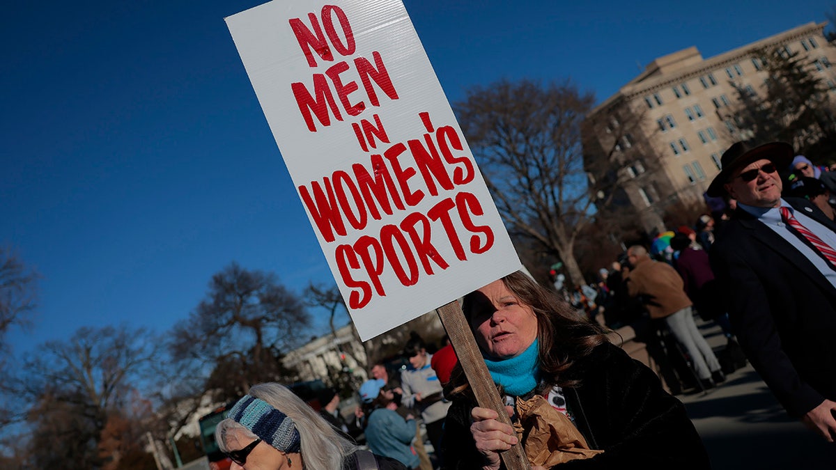 A woman holds a "No men in women's sports" sign
