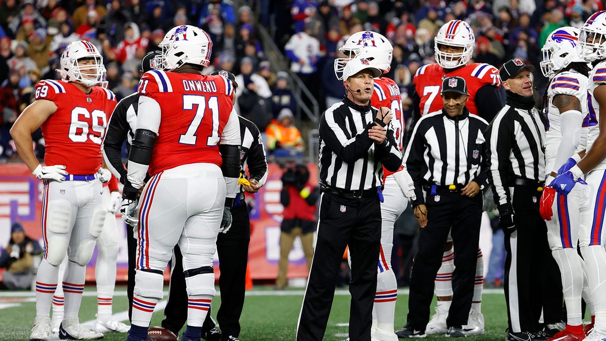 Referee Shawn Hochuli signaling a holding penalty during an NFL game at Gillette Stadium.