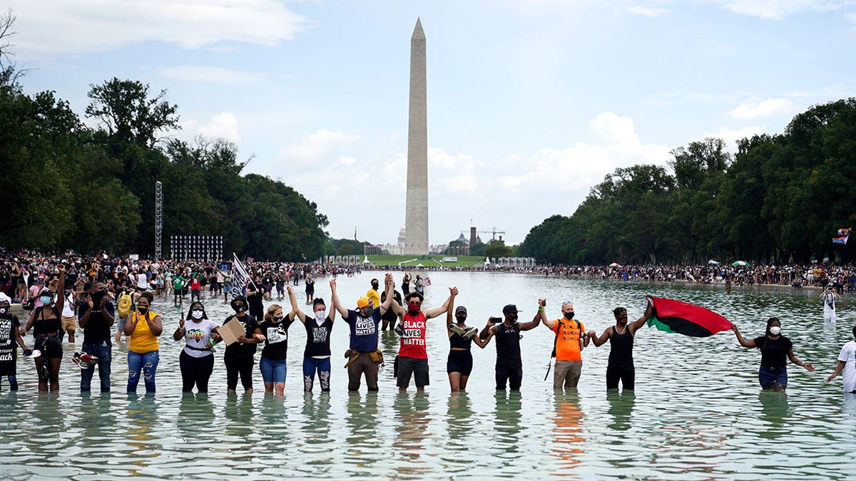 People join hands as they pose for a photo in the Reflecting Pool in the shadow of the Washington Monument.