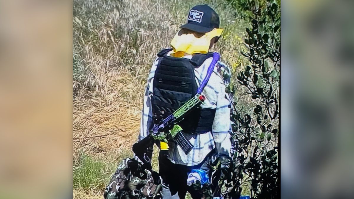 Steiner shown from behind, with the green and purple painted rifle slung from his back