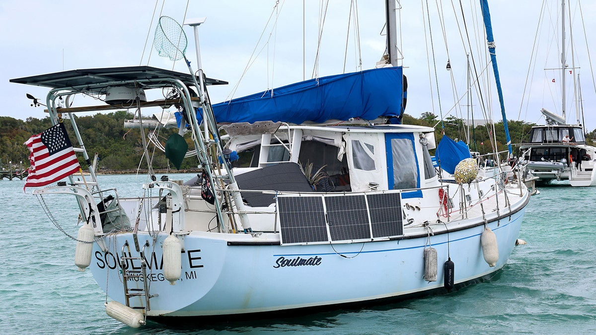 Soulmate boat anchored in calm turquoise water near a shoreline with lush green trees.