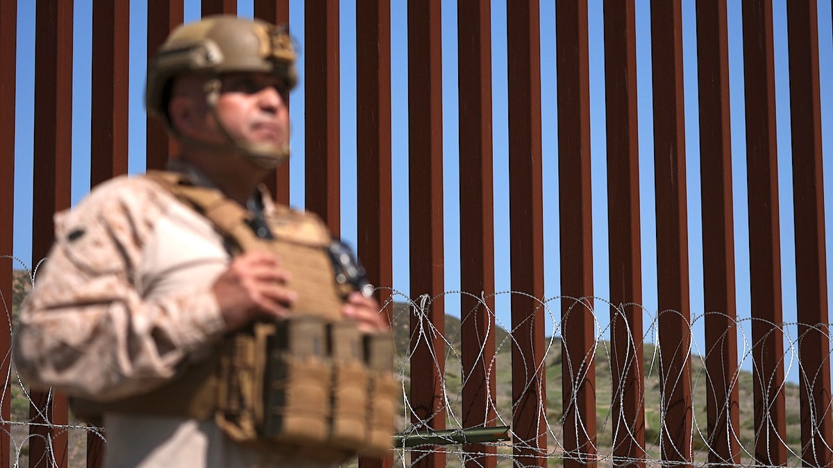 A Marine standing in front of concertina wire on a border wall in San Diego.