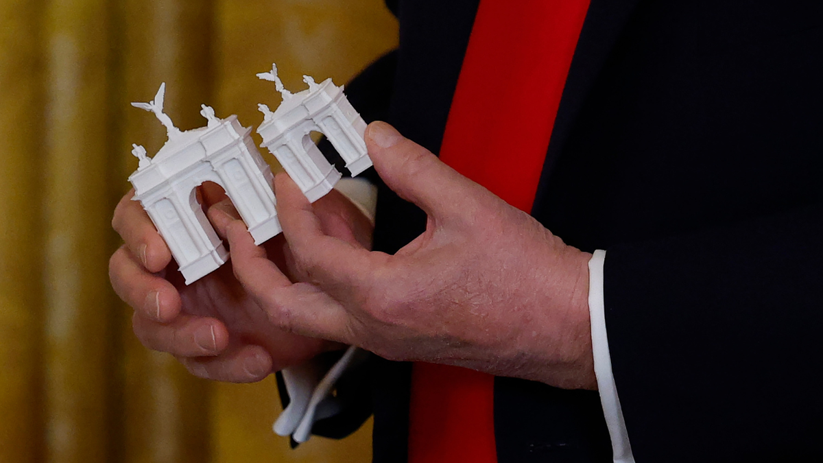President Donald Trump holding models of an arch in the White House East Room.