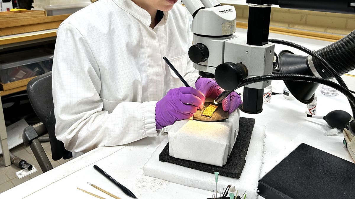 Woman in lab analyzing gold artifact