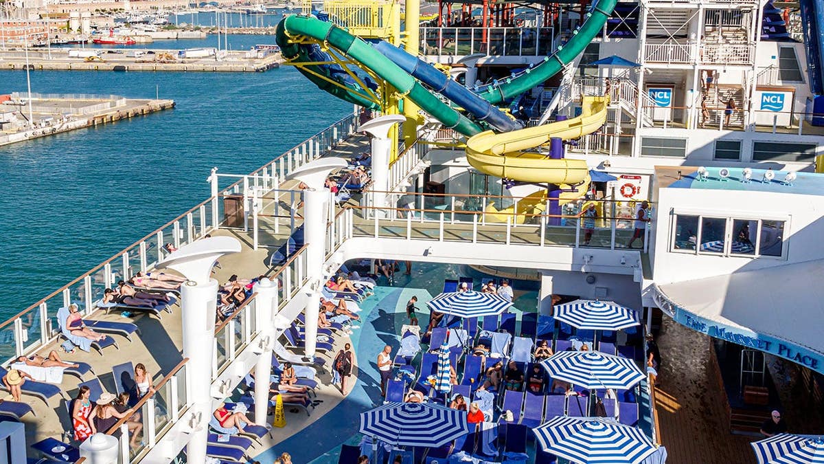 Passengers relaxing on Norwegian Cruise Line pool deck with Civitavecchia city in distance