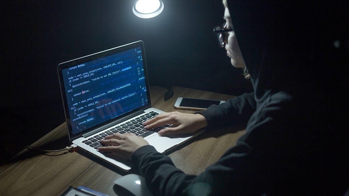 A person in a black sweatshirt hacks a computer in the dark.