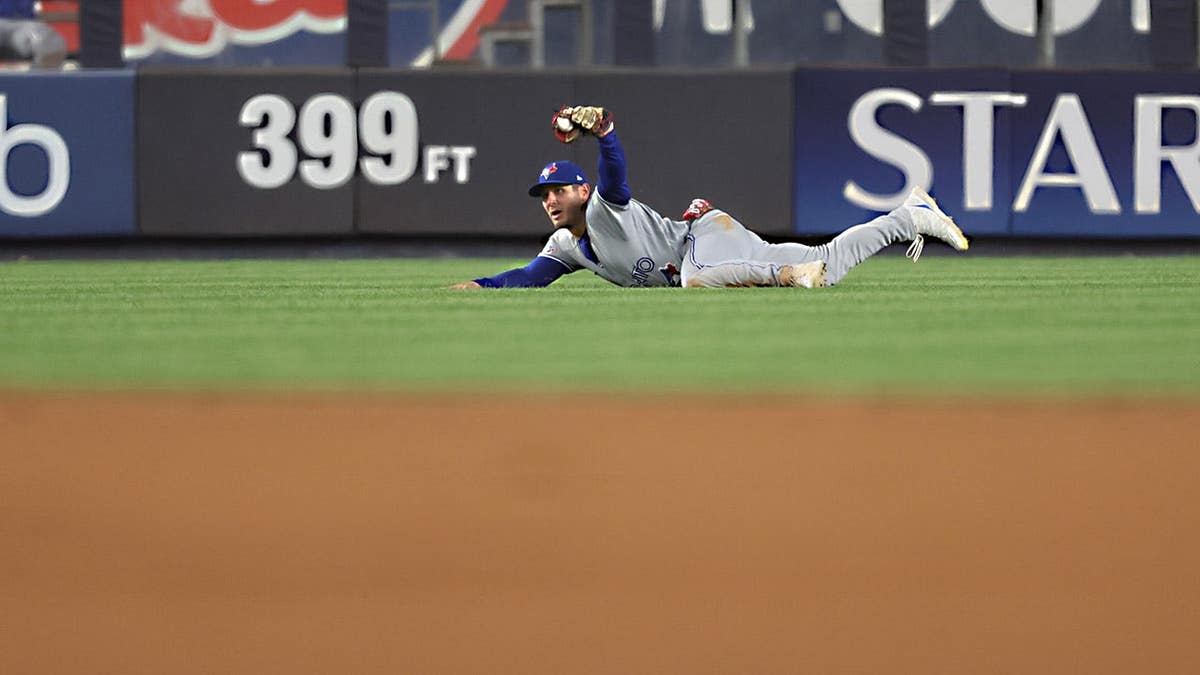 Toronto Blue Jays' Daulton Varsho holding out a baseball during a game.