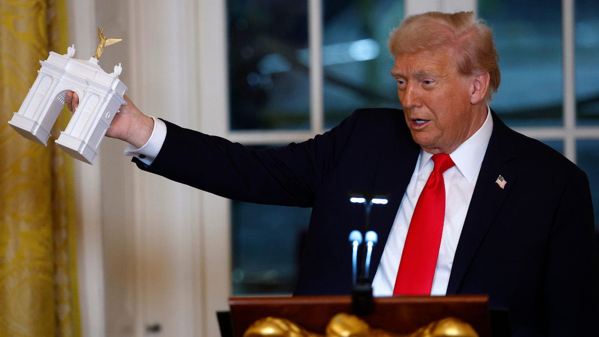 President Donald Trump holding a model of an arch in the White House East Room