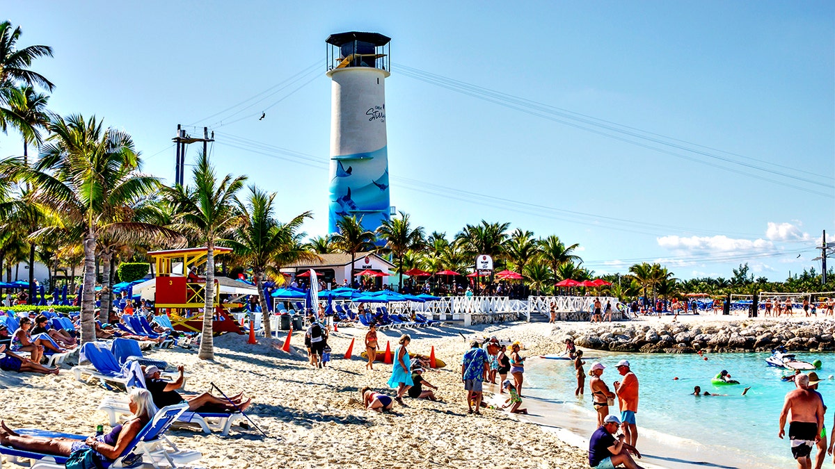 People sunbathing on the beach with a lighthouse tower in the background at Great Stirrup Cay