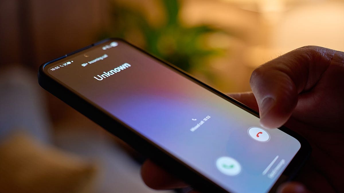 Hand holding smartphone showing unknown incoming call in living room