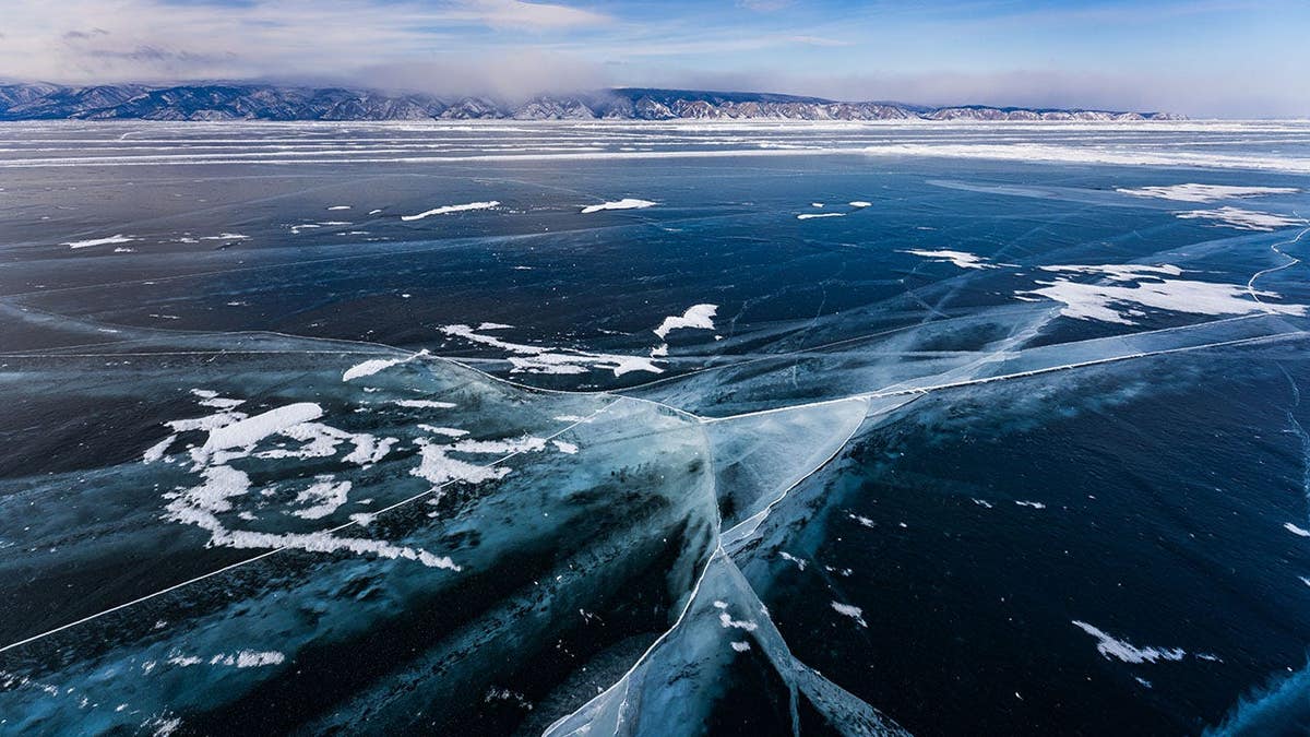 Top-down view of Lake Baikal's frozen surface with intersecting ice cracks and snow spots.