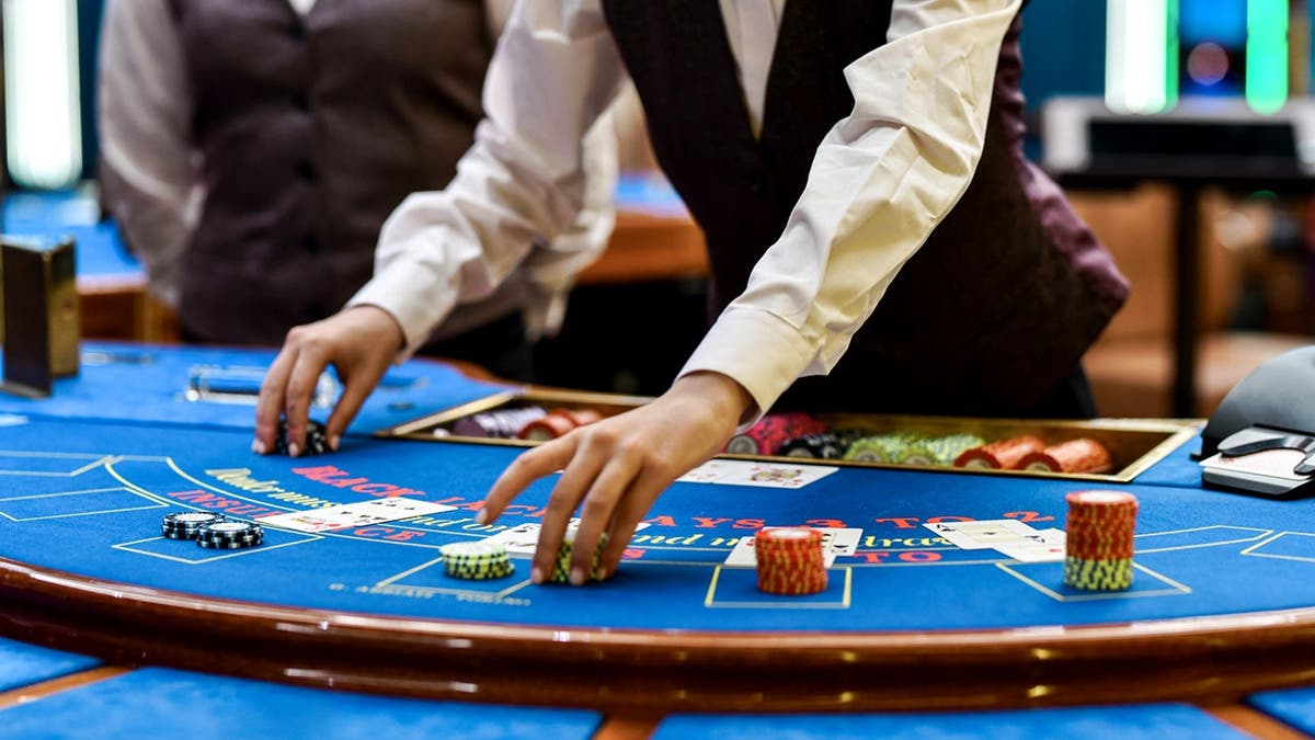 A man stacks up poker chips while dealing a game of Black Jack on a table.