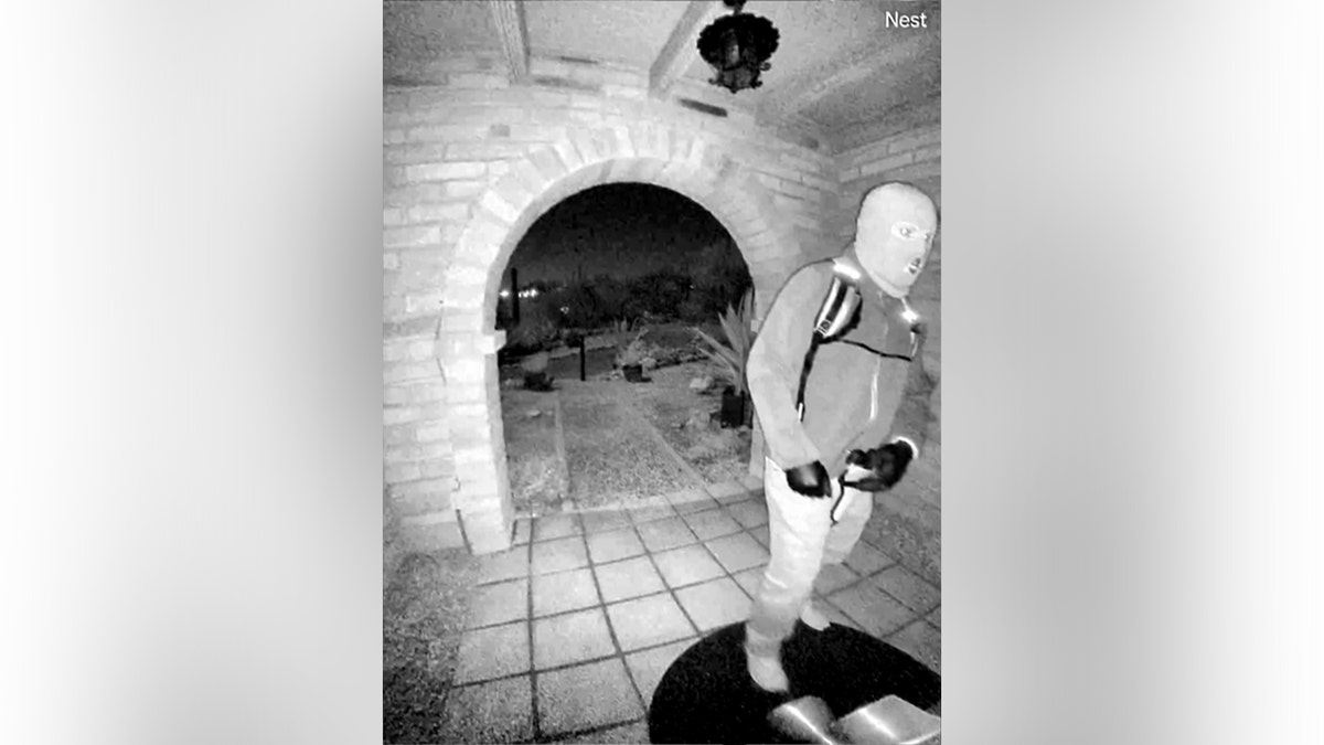 An armed individual reaching toward a Google Nest camera at Nancy Guthrie's front door in Tucson