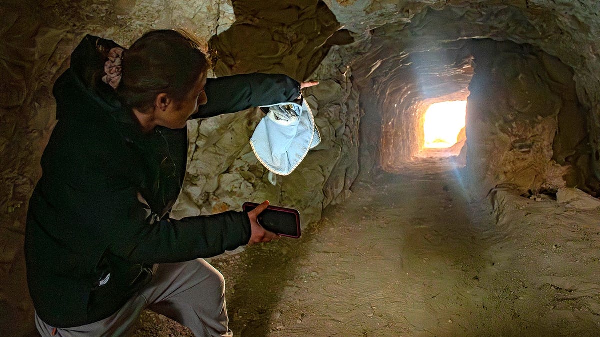 Archaeologist with mask pointing to tunnel