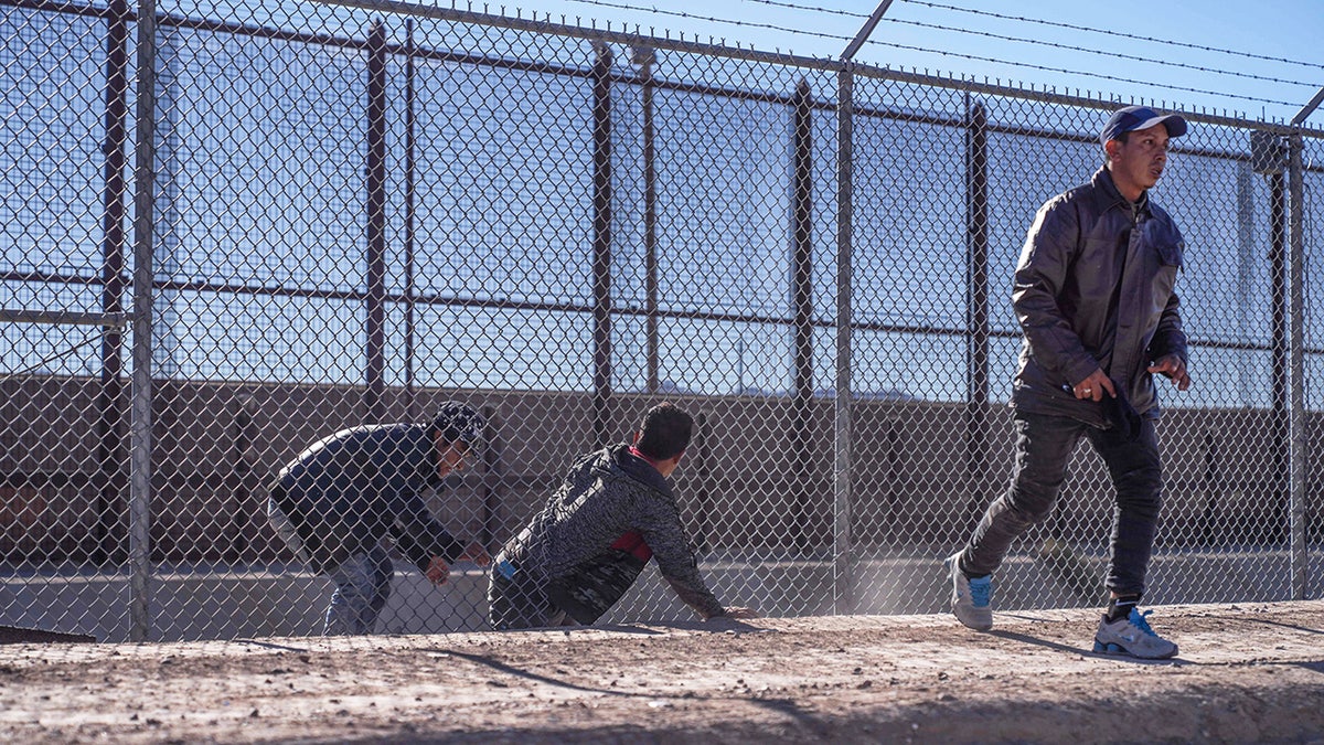 Migrants crossing through a hole in a fence at the Texas border near El Paso