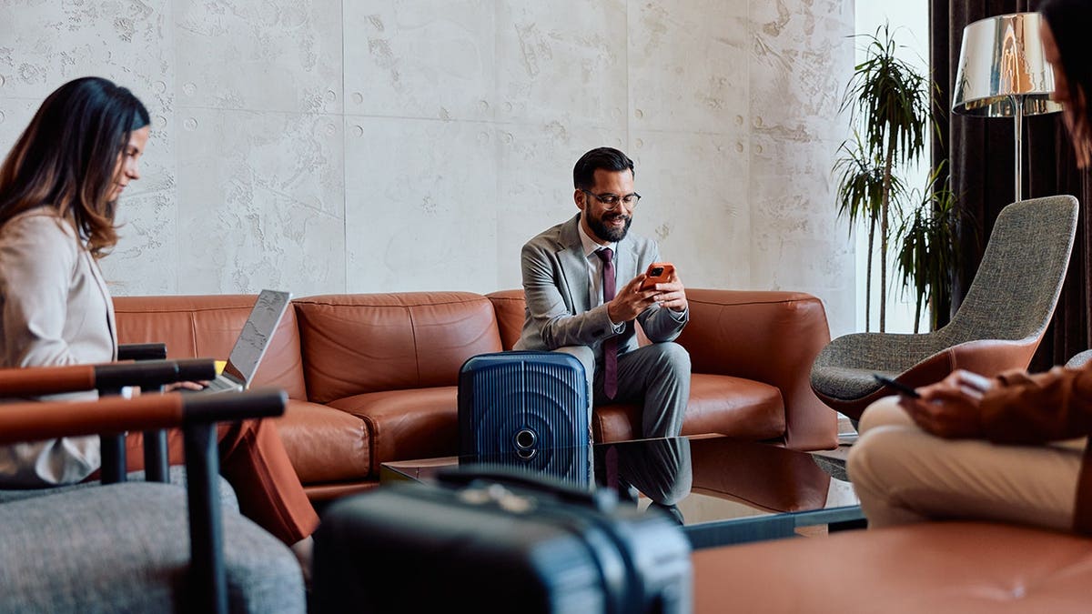Business professionals using smartphones and a laptop in an airport lounge.