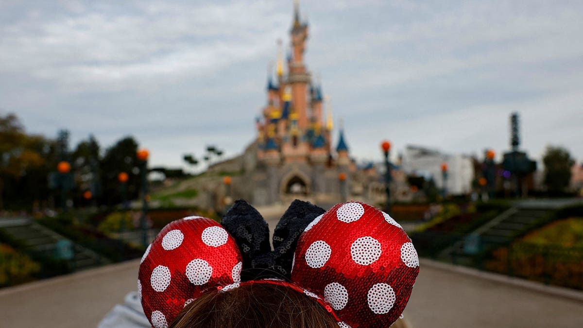 A visitor wearing Mickey and Minnie Mouse ears standing in front of the Sleeping Beauty castle at Disneyland Paris