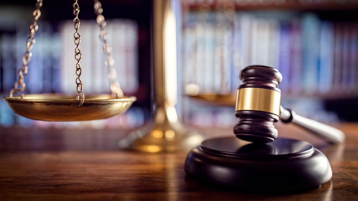 Judge gavel resting on a wooden block with scales of justice and law books in the background