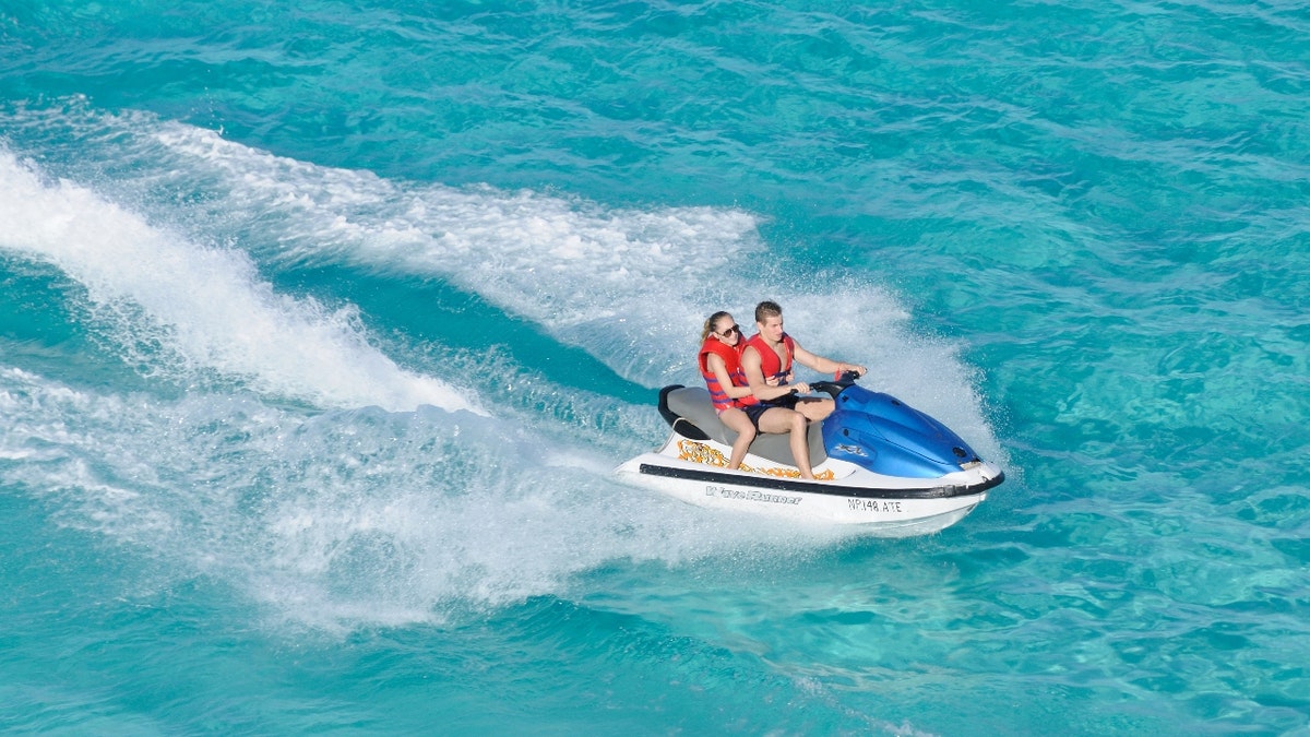 A man and woman riding a jet ski on blue water.