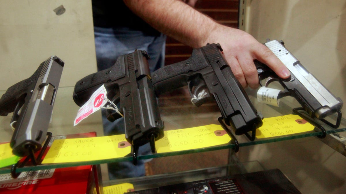 Todd Settergren handling pistols inside a display case at Setterarms gun shop in Walnut Creek, California