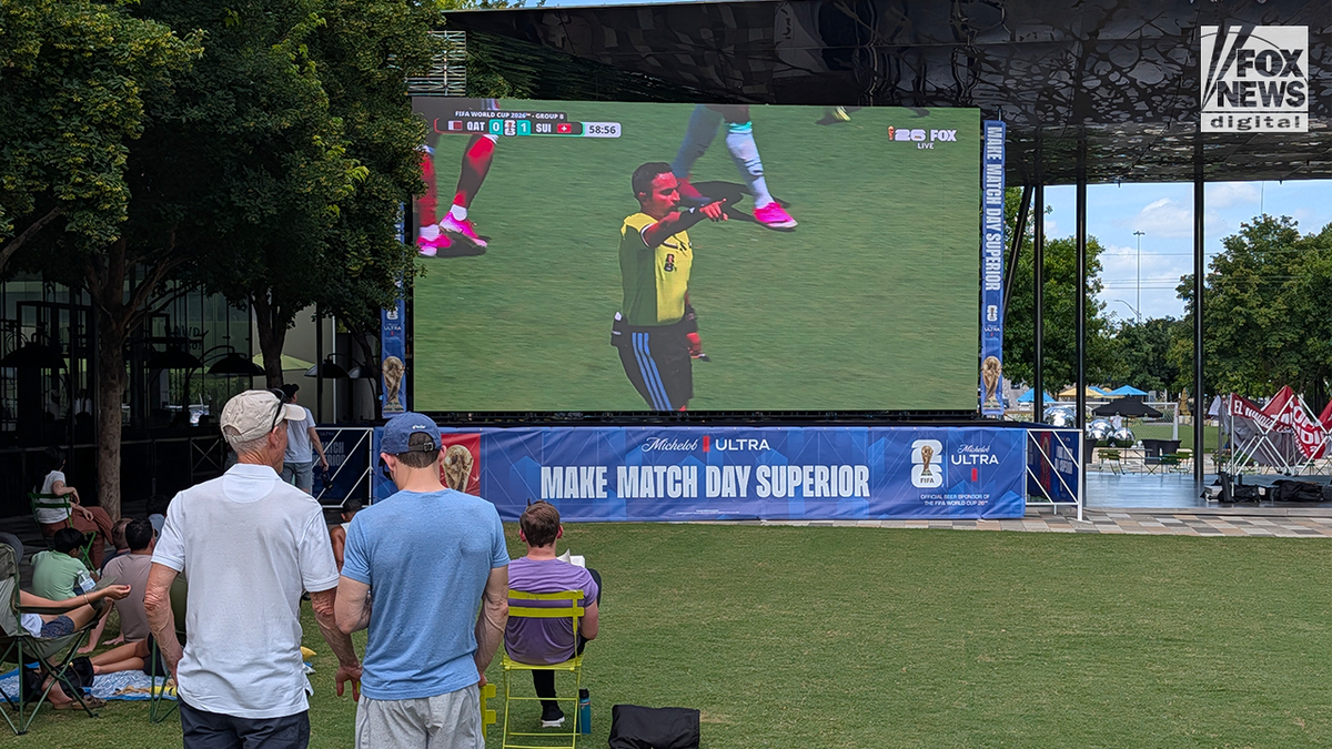 Soccer fans watching a FIFA World Cup match on a giant outdoor screen in a park