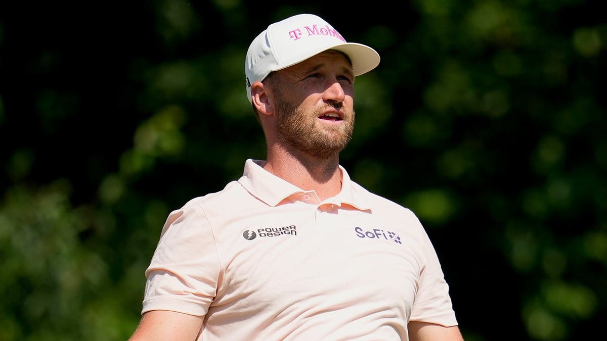 Wyndham Clark watching his tee shot on the 15th hole during a golf tournament.