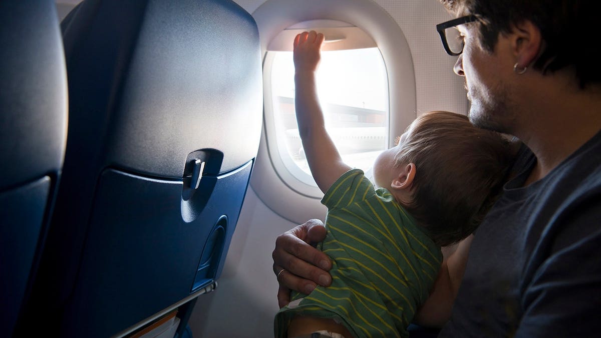 Child sits in a plane seat and looks toward the camera.