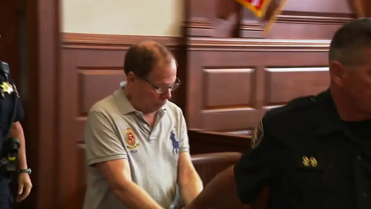 Ronald Fischer walks into a Rhode Island courtroom flanked by sheriff's deputies during his first court appearance after his arrest.