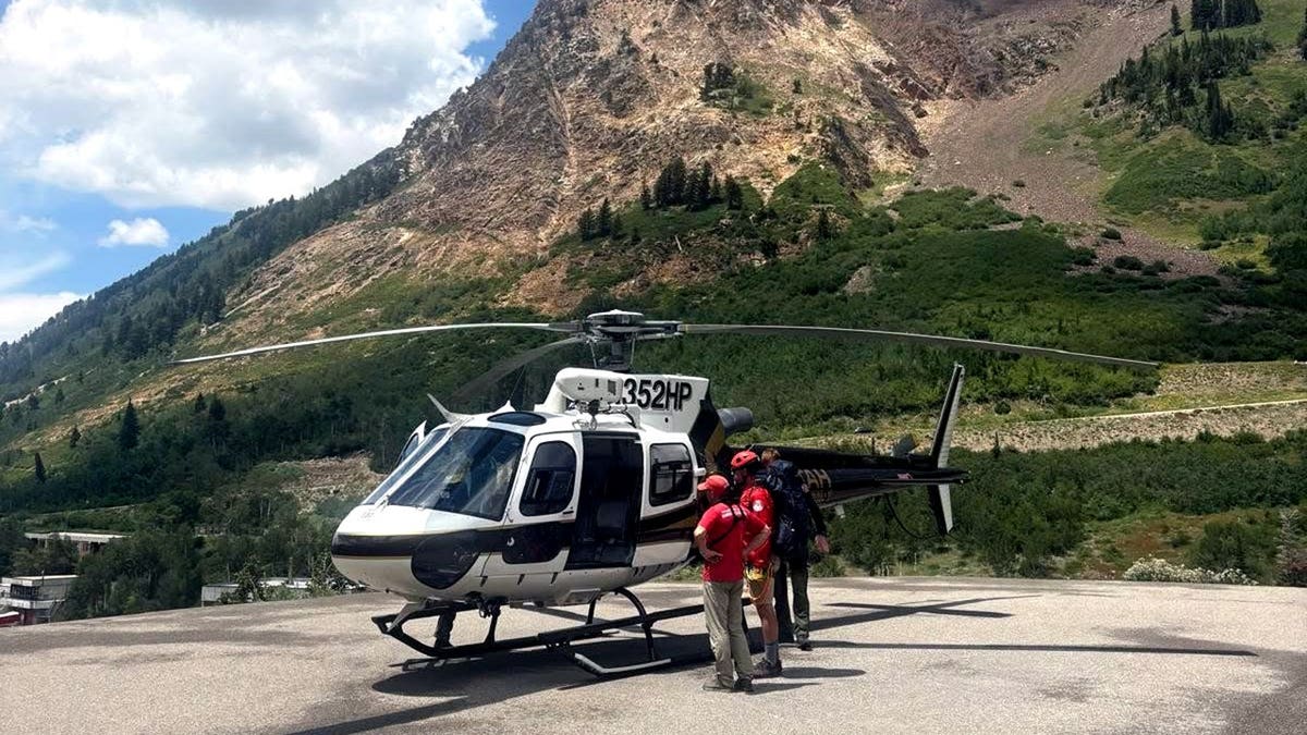 Rescue personnel stand next to a helicopter on a mountain
