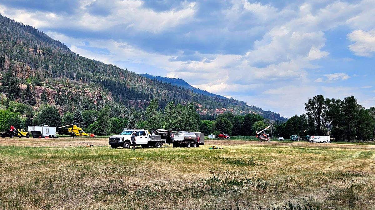 helicopters and emergency vehicles parked in an open field below the moutains
